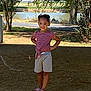 Ava is registered to the contest to win money with this photo: child, girl, outdoor, summer, standing, pond, trees, sunlight, shorts, striped_shirt, sandals, nature, grass, smile, confident, playful, park, daytime, casual_clothing, young