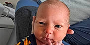 Jayce is registered to the contest to win money with this photo: baby, newborn, infant, face, hands, sweater, person, indoor, bed, fabric, pattern, skin, expression, curious, closeup, holding, adult, cozy, soft, portrait