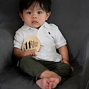 Jason is registered to the contest to win money with this photo: baby, child, infant, polo_shirt, white_shirt, olive_pants, barefoot, armchair, milestone_sign, rhino_illustration, indoor, curious, sitting, portrait, young_child, cute, soft_lighting, black_hair, wide_eyes, person