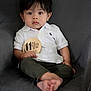 baby, child, infant, polo_shirt, white_shirt, olive_pants, barefoot, armchair, milestone_sign, rhino_illustration, indoor, curious, sitting, portrait, young_child, cute, soft_lighting, black_hair, wide_eyes, person