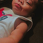 Kylin is registered to the contest to win money with this photo: baby, infant, child, face, arm, sleeveless_shirt, textile, portrait, skin, lying_down, closeup, expression, indoors, dark_background, noise, grainy, casual_clothing, young_child, resting, person