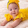 baby, infant, smiling, yellow_dress, headband, flower, blanket, soft_texture, cute, portrait, happy, lying_down, indoors, child, toddler, bright_colors, warm_lighting, bokeh, close_up, adorable