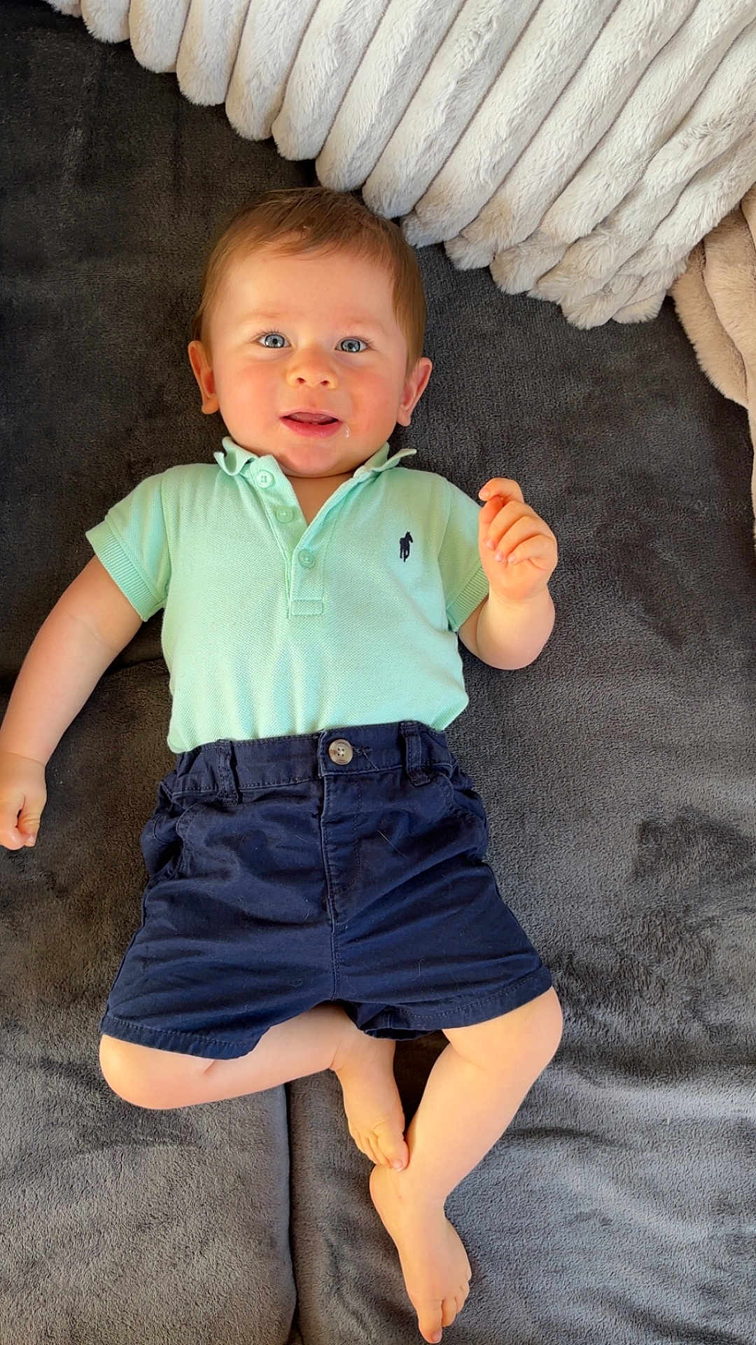 Aloïs a rejoint le concours — aidez-le/la à gagner de superbes lots ! baby, child, infant, polo_shirt, shorts, blue_eyes, smiling, lying_down, blanket, pillow, soft_texture, indoor, cute, happy, person, casual_clothing, feet, hand, portrait, toddler