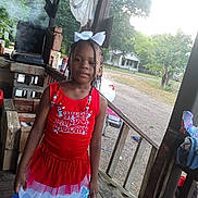 La'Kerria joined the competition — help win amazing prizes! child, girl, portrait, smiling, patriotic, red_dress, blue_dress, white_bow, braids, outdoor, porch, wooden_porch, grill, smoke, house, yard, trees, road, rural, daylight