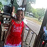 child, girl, portrait, smiling, patriotic, red_dress, blue_dress, white_bow, braids, outdoor, porch, wooden_porch, grill, smoke, house, yard, trees, road, rural, daylight