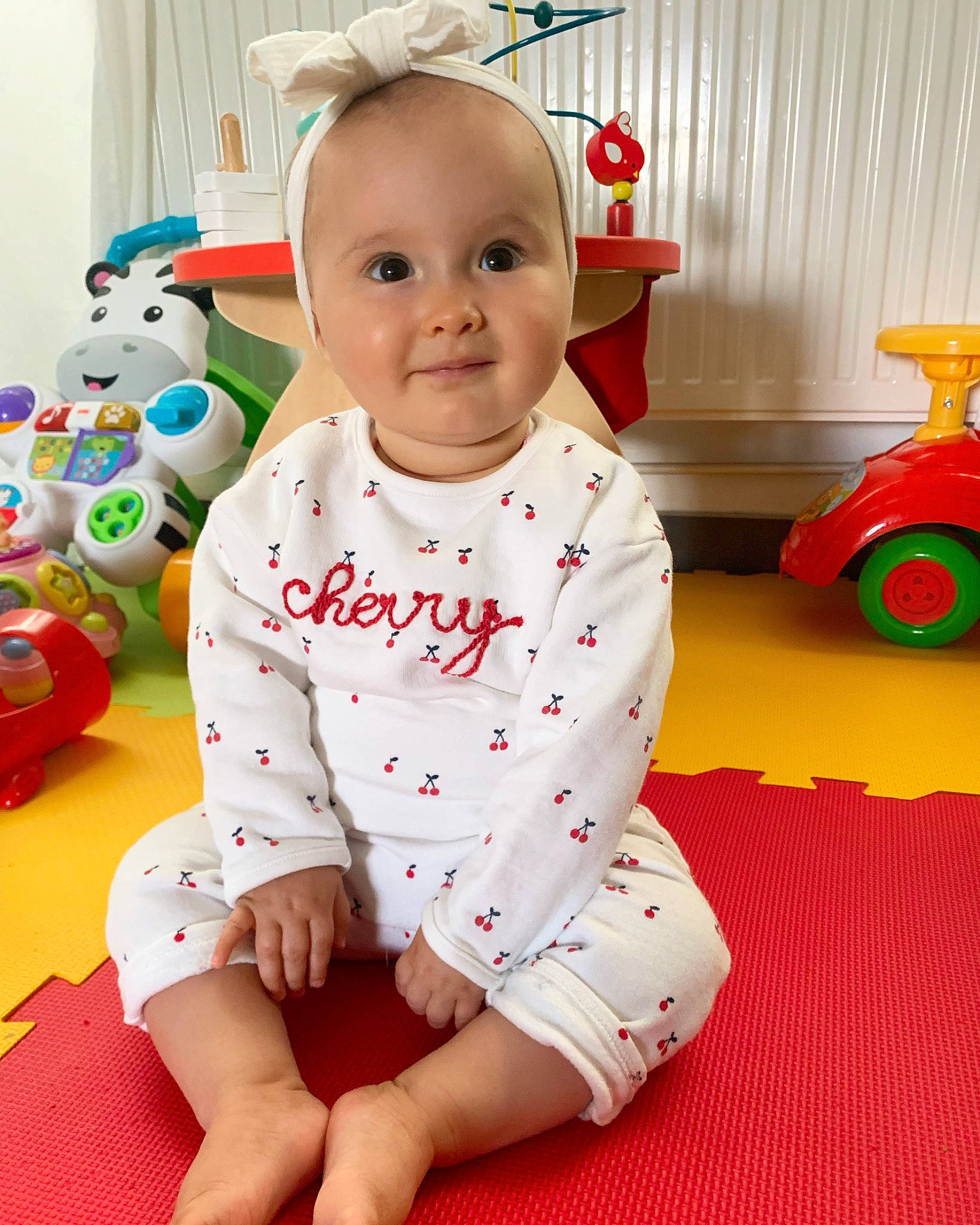 Lila a rejoint le concours — aidez-le/la à gagner de superbes lots ! baby, baby_toddler_clothing, cheek, face, facial_expression, floor, flooring, happy, joy, person, product, red, skin, sleeve, smile, standing, t_shirt, tire, toddler, wheel