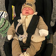 Eddie is registered to the contest to win money with this photo: baby, infant, car_seat, sleeping, hat, mickey_mouse, pom_pom, clothing, mittens, socks, plush_toy, zebra, blanket, safety_harness, indoor, cute, cozy, child, person, resting