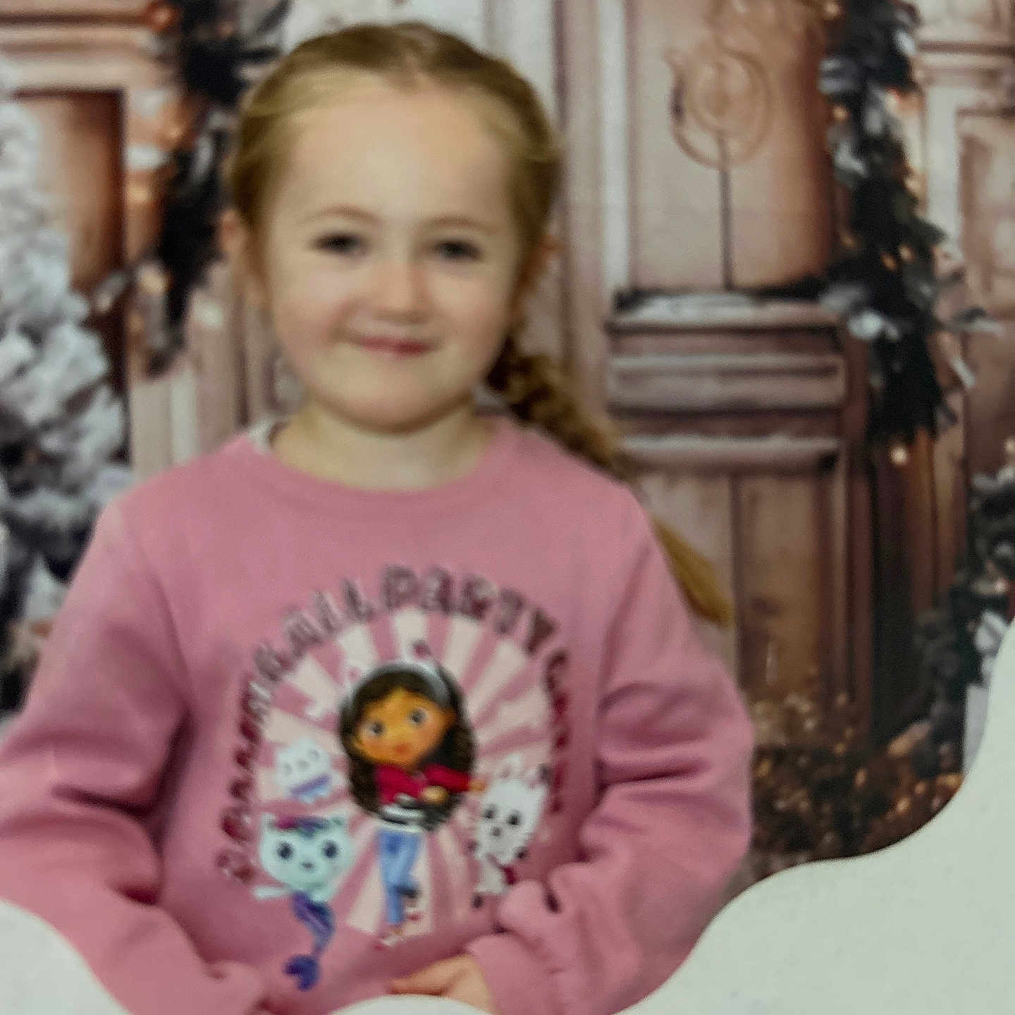 Giulia is registered to the contest to win money with this photo: child, girl, smile, pink_sweatshirt, cartoon_characters, braided_hair, portrait, indoor, festive_background, blurred_background, young_person, happy, casual_clothing, face, person, childhood, cute, cozy, warm_colors, photograph