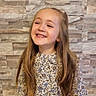 Giulia participe au concours pour gagner de l'argent avec cette photo : background, casual, child, cute, face, fashion, floral_dress, girl, happy, indoor, joyful, light, long_hair, patterned_clothing, person, portrait, smiling, standing, stone_wall, young