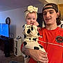 baby, child, man, person, indoor, living_room, television, carpet, clothing, headband, tattoo, smile, holding, hand, furniture, young_adult, casual, portrait, happy, people