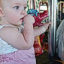 baby, child, toddler, carousel, amusement_ride, pink_clothing, white_tank_top, hand_on_mouth, curious, portrait, indoor, decorative, face, side_view, bright_lights, amusement_park, playful, young_child, sitting, holding_pole