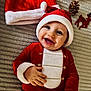 baby, celebration, child, christmas_outfit, cute, festive, happy, holiday, holiday_decorations, indoor, infant, lying_down, pine_cone, portrait, red_clothing, santa_hat, seasonal, smiling, toy, white_fur_trim