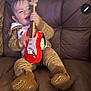 Noah is registered to the contest to win money with this photo: child, toddler, toy_guitar, brown_pajamas, leather_couch, indoor, smiling, playing, happy, footwear, baby, cozy, cute, music, fun, person, sitting, home, entertainment, expression