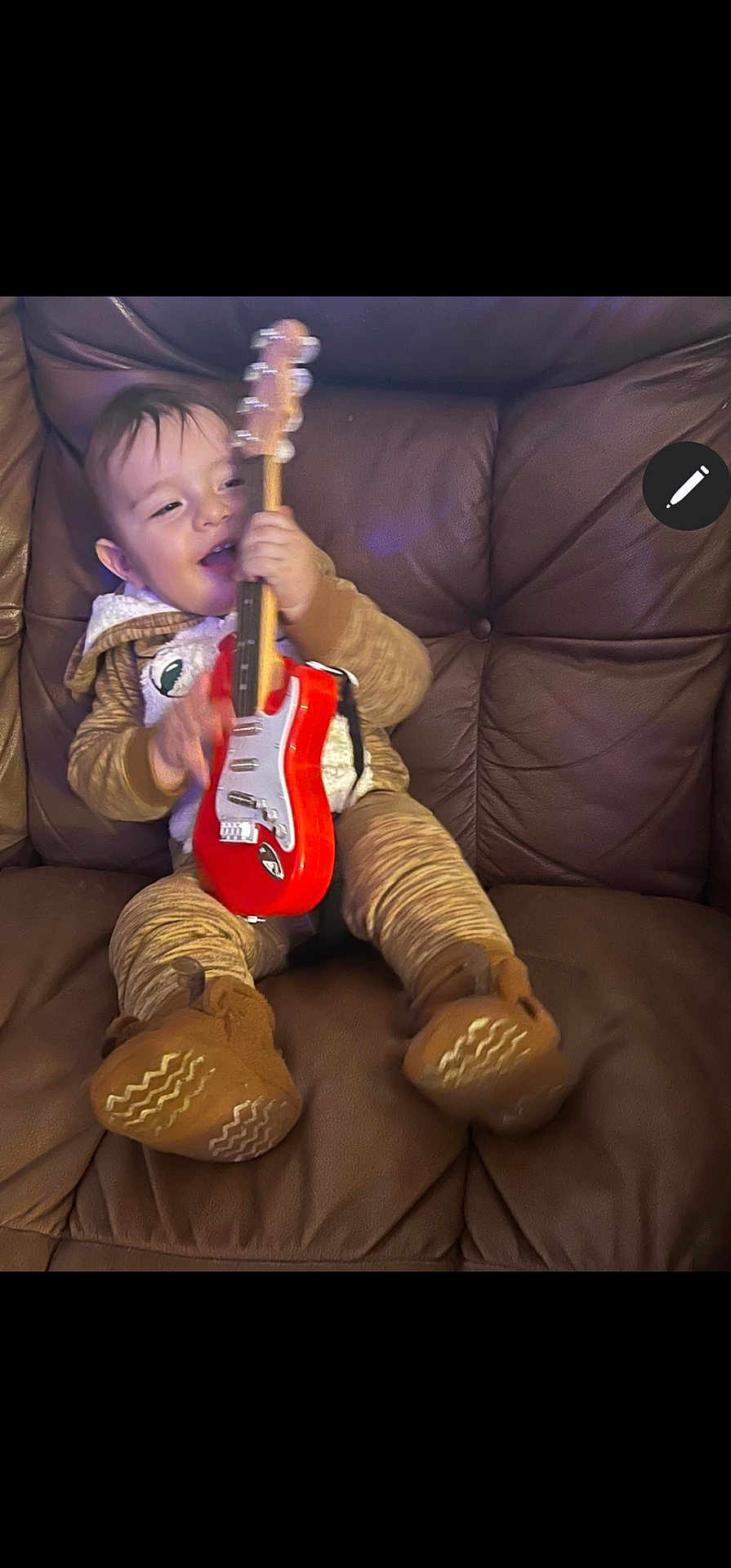 Noah is registered to the contest to win money with this photo: child, toddler, toy_guitar, brown_pajamas, leather_couch, indoor, smiling, playing, happy, footwear, baby, cozy, cute, music, fun, person, sitting, home, entertainment, expression