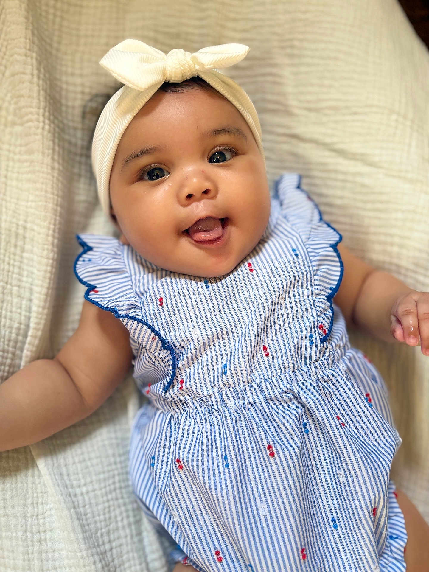 Nara joined the competition — help win amazing prizes! baby, infant, child, smiling, headband, bow, dress, striped_clothing, cute, lying_down, blanket, soft_texture, happy, portrait, closeup, cheeks, tongue, skin, arm, indoors