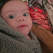 Raven is registered to the contest to win money with this photo: baby, blanket, face, fuzzy, curious, wide_eyes, indoor, portrait, child, soft_texture, warmth, snug, clothing, cozy, infant, close_up, expression, comfort, resting, young