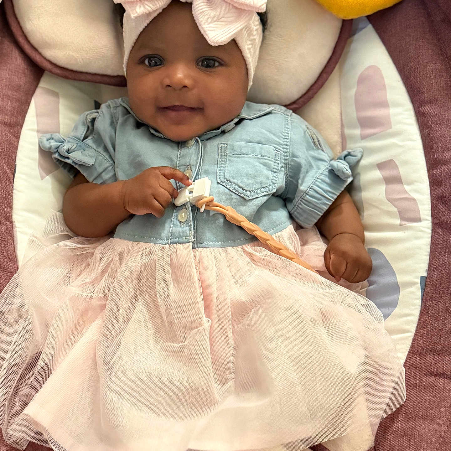 Azariyah Kai joined the competition — help win amazing prizes! baby, infant, child, smile, headband, bow, dress, tutu, denim, clothing, cushion, plush_toy, blue, yellow, pink, cute, portrait, indoors, person, lying_down