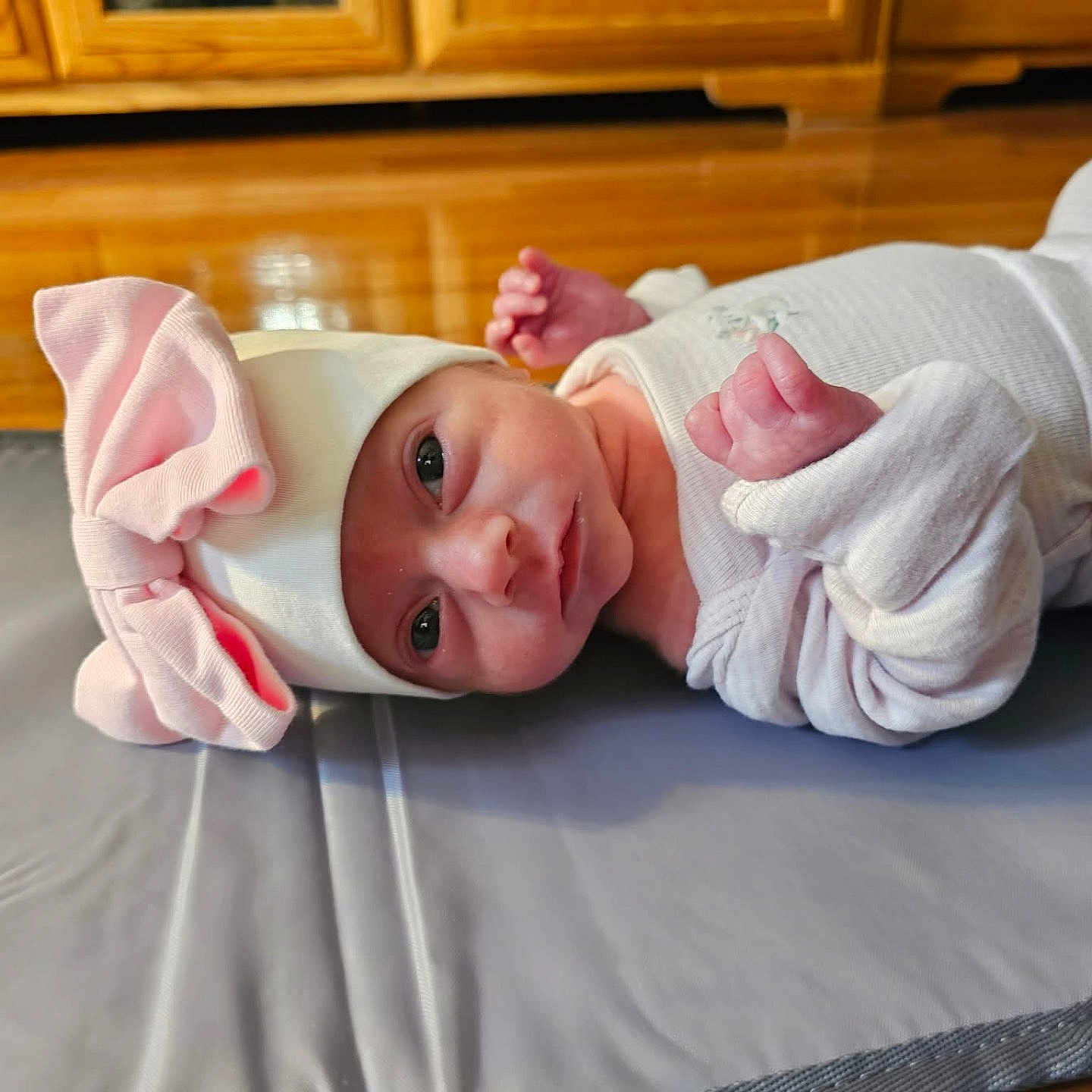 Rylee is registered to the contest to win money with this photo: awake, baby, bow, child, cozy, cute, face, furniture, hat, indoor, infant, lying_down, mat, newborn, pink, portrait, small_hands, soft_lighting, white_clothing, wooden_floor