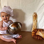 Elyo participe au concours pour gagner de l'argent avec cette photo : apron, baby, baguette, baking, bread, chef_hat, child, cooking, croissant, cute, food, happy, indoors, kitchen, mixing_bowl, pastry, sitting, smiling, white_background, wooden_spoon