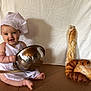 apron, baby, baguette, baking, bread, chef_hat, child, cooking, croissant, cute, food, happy, indoors, kitchen, mixing_bowl, pastry, sitting, smiling, white_background, wooden_spoon