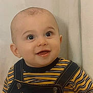 Gio is registered to the contest to win money with this photo: baby, child, smiling, face, eyes, clothing, striped_shirt, overalls, portrait, indoor, happy, cute, infant, closeup, head, skin, person, young_child, background, expression