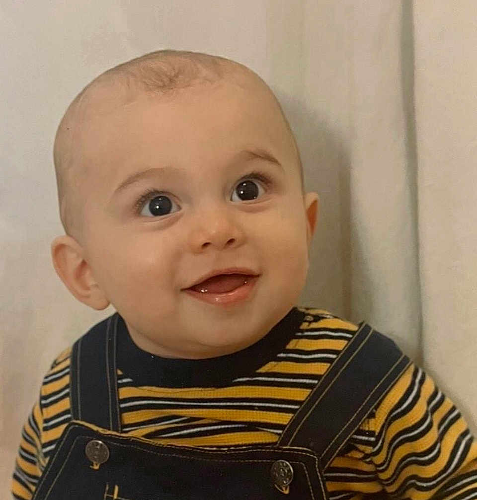 Gio is registered to the contest to win money with this photo: baby, child, smiling, face, eyes, clothing, striped_shirt, overalls, portrait, indoor, happy, cute, infant, closeup, head, skin, person, young_child, background, expression