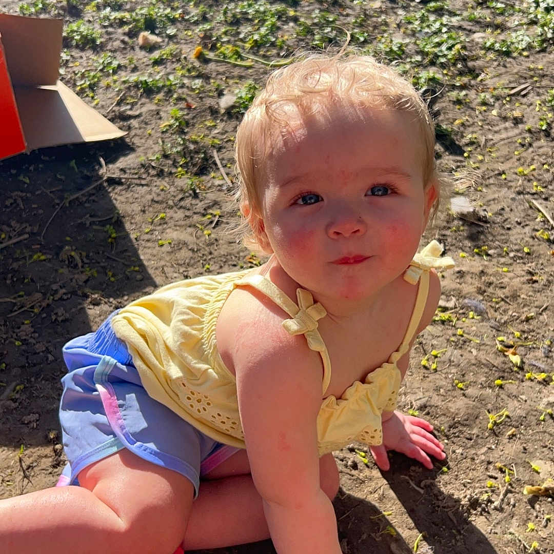 Milayah is registered to the contest to win money with this photo: baby, backyard, clothing, dress, face, footwear, grass, head, nature, outdoors, person, photography, plant, playarea, portrait, shoe, shorts, sitting, soil, yard