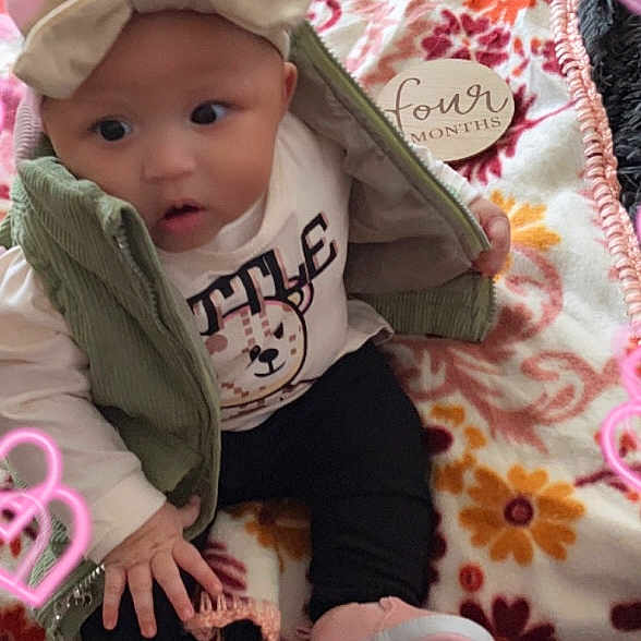 Na Veyah is registered to the contest to win money with this photo: adorable, baby, black_pants, bow_headband, carpet, child, clothing, cute, floral_blanket, four_months_tag, green_vest, heart_overlay, indoor, infant, pink_shoes, playful, portrait, sitting, white_shirt, young_child