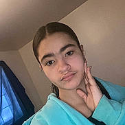 Aniya joined the competition — help win amazing prizes! person, young_person, indoor, face, hand, hoodie, casual_clothing, window, curtain, neutral_expression, portrait, wall, hair, sitting, relaxed, natural_light, home, youth, skin, eyebrows