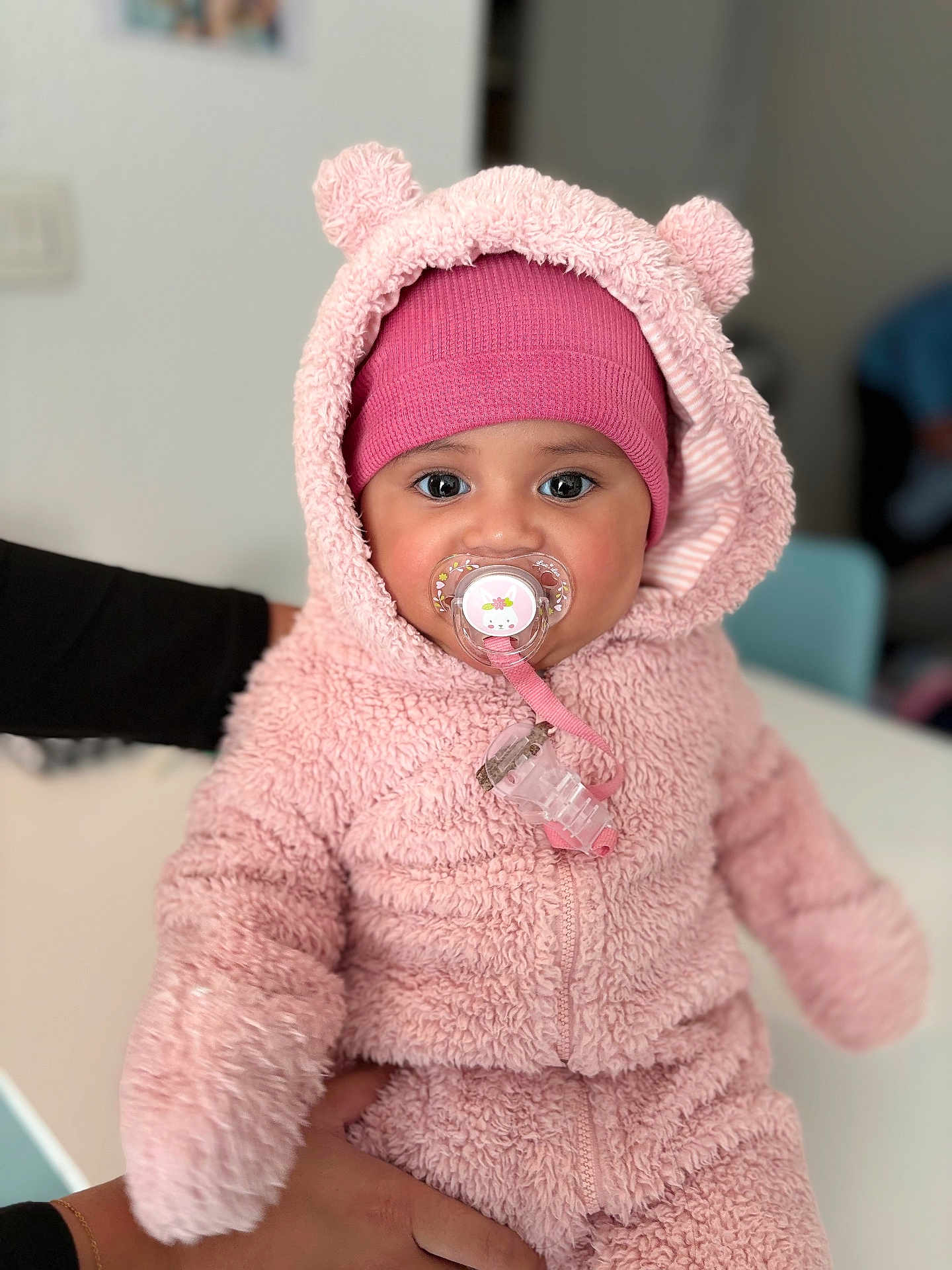 Kaiulani a rejoint le concours — aidez-le/la à gagner de superbes lots ! baby, child, pacifier, pink_clothing, hood, beanie, cute, fluffy, indoor, person, face, portrait, warm_clothing, hand, soft_texture, infant, adorable, looking_at_camera, close_up, seated