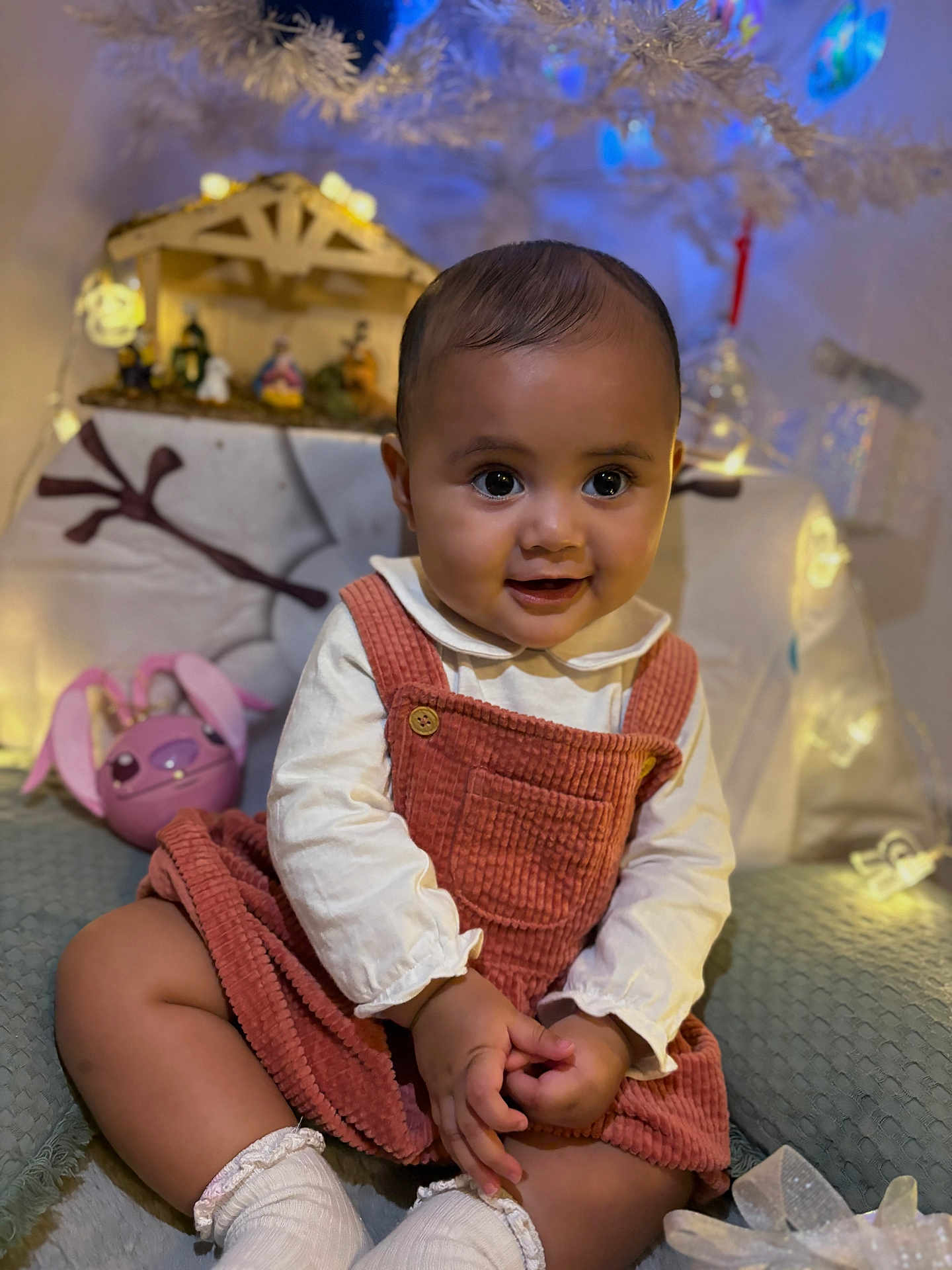 Kaiulani participe au concours pour gagner de l'argent avec cette photo : baby, child, corduroy, cozy, cute, decorations, dress, face, festive, hands, happy, holiday_lights, indoors, infant, portrait, sitting, smiling, socks, warm_lighting, white_blouse