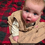 Brynlee is registered to the contest to win money with this photo: baby, beige, black, blanket, child, clothing, curious, cute, expression, face, indoors, infant, person, plaid, portrait, red, rosy_cheeks, sitting, surprise, young