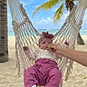 baby, infant, hammock, beach, sand, palm_tree, ocean, sky, clouds, hand, grape, headband, pink_pants, floral_top, white_socks, relaxation, tropical, vacation, outdoor, nature