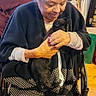 Hope joined the competition — help win amazing prizes! elderly_woman, black_cat, wheelchair, indoor, person, man, doll, wooden_floor, window, curtain, sweater, long_hair, glasses, nail_polish, holding, seated, cozy, home, furniture, casual_clothing