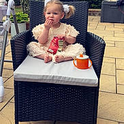 Amelia joined the competition — help win amazing prizes! toddler, child, outdoor, wicker_chair, snack, sippy_cup, pigtails, cushion, patio, plants, fence, table, footwear, clothing, person, hair_bow, greenery, relaxing, daytime, cute