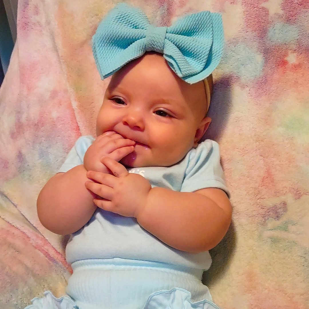 Irismae is registered to the contest to win money with this photo: baby, blue_bow, cheeks, child, chubby, comfortable, cozy, cute, fingers, happy, headband, indoors, infant, light_blue_clothing, pastel_blanket, portrait, sitting, smile, soft_texture, young_child