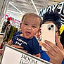 Devonte is registered to the contest to win money with this photo: baby, bright, casual, child, clothing, face, hand, head, holding, indoor, mirror, person, phone, reflection, selfie, shopping, sign, smiling, store, text