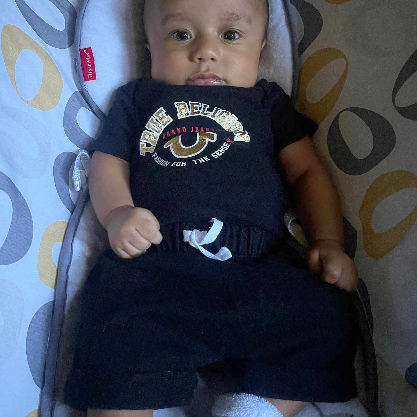 Kirk joined the competition — help win amazing prizes! baby, infant, child, face, person, black_clothing, socks, baby_seat, patterned_background, fisher_price, cute, indoors, portrait, looking_at_camera, cozy, small_hands, sitting, casual, curious, young