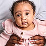 baby, child, pink_bow, pink_clothing, curly_hair, droplet, hands, adult_hands, portrait, close_up, cute, expression, indoor, soft_lighting, face, eyes, infant, person, holding, adorable