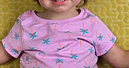 Riley is registered to the contest to win money with this photo: toddler, child, smiling, portrait, indoors, seated, yellow_background, patterned_cushion, pink_shirt, palm_tree_pattern, black_shorts, brown_hair, blue_eyes, missing_teeth, happy, front_facing, close_up, casual_clothing, family_photo, photography