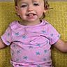 toddler, child, smiling, portrait, indoors, seated, yellow_background, patterned_cushion, pink_shirt, palm_tree_pattern, black_shorts, brown_hair, blue_eyes, missing_teeth, happy, front_facing, close_up, casual_clothing, family_photo, photography