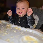 Riley is registered to the contest to win money with this photo: baby, child, high_chair, food, messy, happy, blue_eyes, smile, face, hands, clothing, indoor, meal, feeding, cute, infant, porridge, kitchen, table, tray