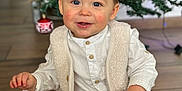 Ysao participe au concours pour gagner de l'argent avec cette photo : toddler, child, baby, smile, blue_eyes, rosy_cheeks, white_shirt, beige_vest, brown_pants, white_shoes, christmas_tree, ornaments, holiday, indoor, wooden_floor, festive, happy, sitting, cute, portrait