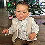 toddler, child, baby, smile, blue_eyes, rosy_cheeks, white_shirt, beige_vest, brown_pants, white_shoes, christmas_tree, ornaments, holiday, indoor, wooden_floor, festive, happy, sitting, cute, portrait