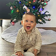 Ysao a rejoint le concours — aidez-le/la à gagner de superbes lots ! baby, child, smiling, sitting, floor, christmas_tree, ornaments, holiday, festive, indoors, clothing, shoes, happy, cute, young_child, decoration, celebration, person, portrait, wooden_floor
