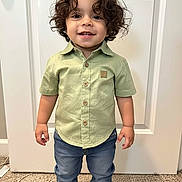 Jonathan is registered to the contest to win money with this photo: toddler, child, curly_hair, smiling, standing, indoor, shirt, jeans, footwear, door, carpet, button_up_shirt, happy, person, cute, young_child, casual_clothing, full_body, portrait, home
