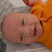 Gabriel a rejoint le concours — aidez-le/la à gagner de superbes lots ! baby, smiling, infant, orange_shirt, face, head, eyes, mouth, clothing, fabric, portrait, closeup, happy, child, skin, cute, person, laying_down, indoors, young