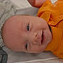baby, smiling, infant, orange_shirt, face, head, eyes, mouth, clothing, fabric, portrait, closeup, happy, child, skin, cute, person, laying_down, indoors, young