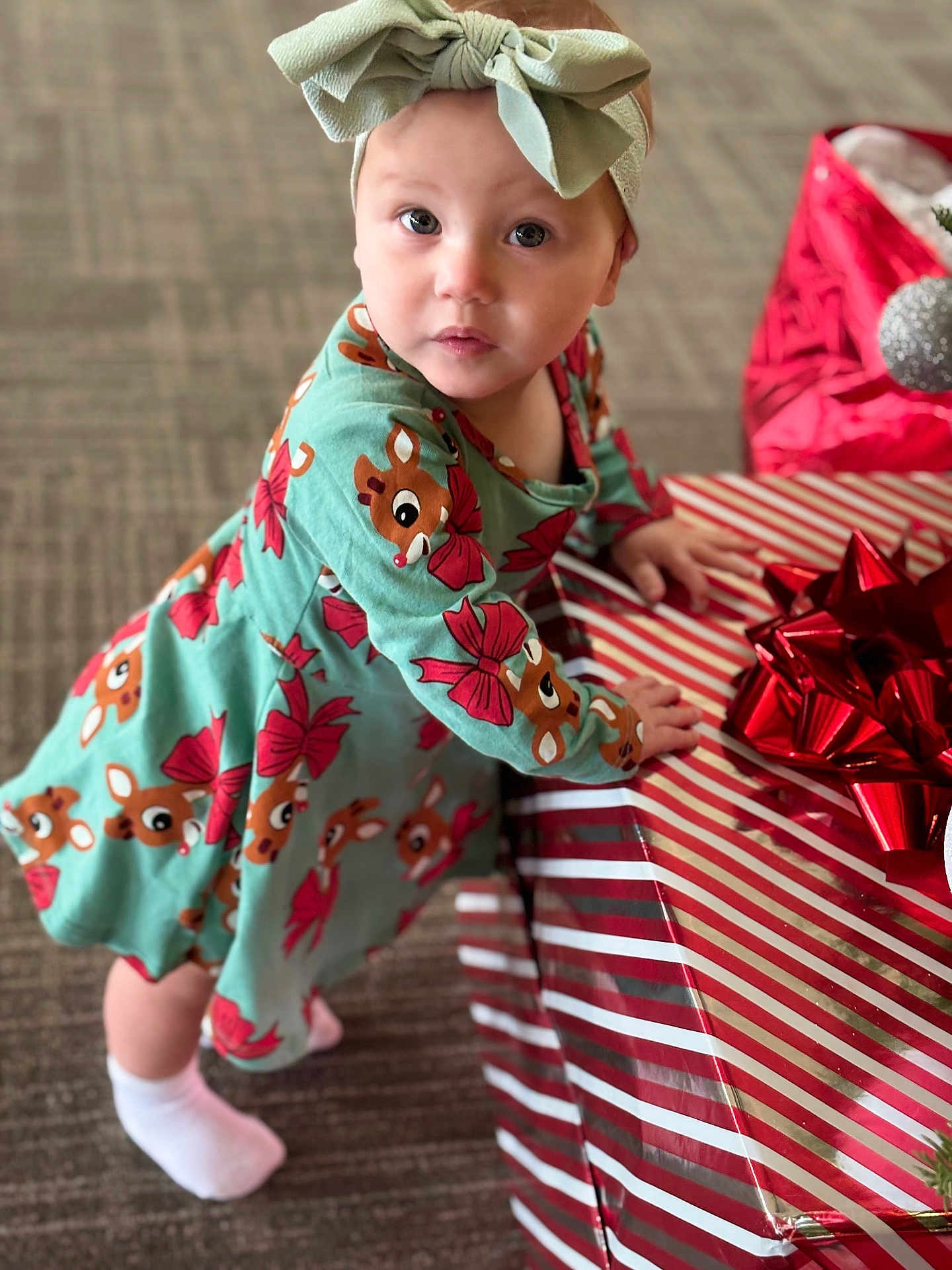 Araia is registered to the contest to win money with this photo: toddler, child, present, gift, holiday, christmas, reindeer, dress, headband, bow, socks, carpet, indoor, cute, curious, holiday_theme, festive, wrapped_gift, red, green