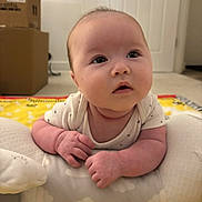 Bella is registered to the contest to win money with this photo: baby, infant, child, cushion, face, indoors, carpet, cardboard_box, curious, expression, hands, play_mat, soft_toy, tummy_time, white_clothing, room, window_blinds, floor, skin, head